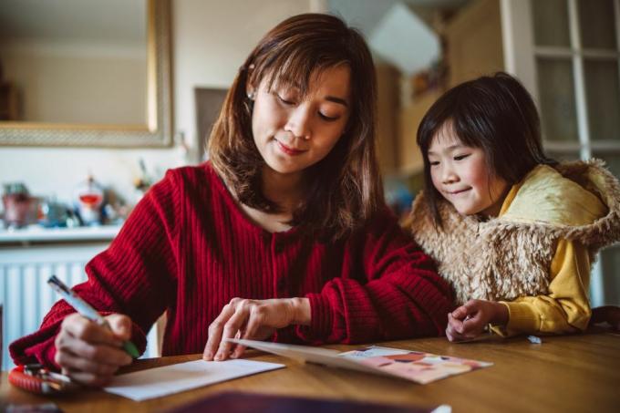 Una joven y bonita madre escribiendo una tarjeta de felicitación para la familia con su encantadora hija en casa