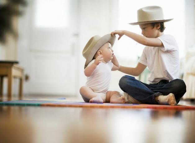 enfoque selectivo vista de dos hermanos, uno tiene nueve años uno tiene ocho meses la pareja se sienta con las piernas cruzadas en el suelo el niño mayor pone un sombrero a juego en la cabeza del bebé