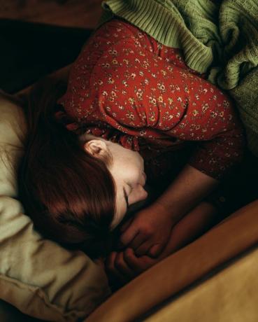 retrato de una mujer pelirroja cubierta con una manta verde tumbada en el sofá amarillo y durmiendo en otoño o invierno, ambiente cálido y acogedor tomando café por la mañana