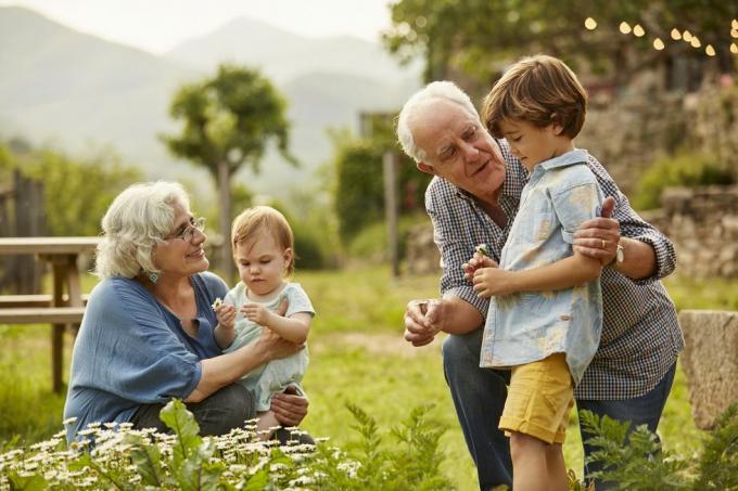 abuelos hablando con dos niños pequeños en el patio con montañas y casa en segundo plano