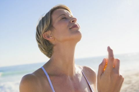 Mujer rociando perfume en su cuello en la playa.