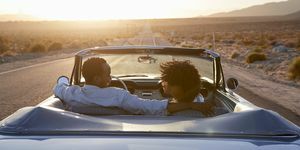 vista trasera de una pareja en un viaje por carretera conduciendo un coche convertible clásico hacia el atardecer