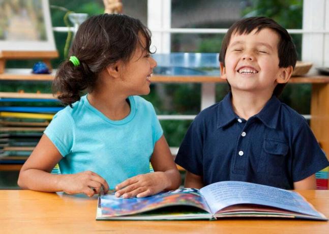 dos niños riendo disfrutando de un libro en la escuela