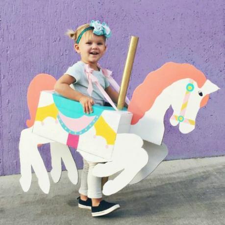 niña con una caja en forma y pintada para parecerse a un carrusel de caballos a su alrededor