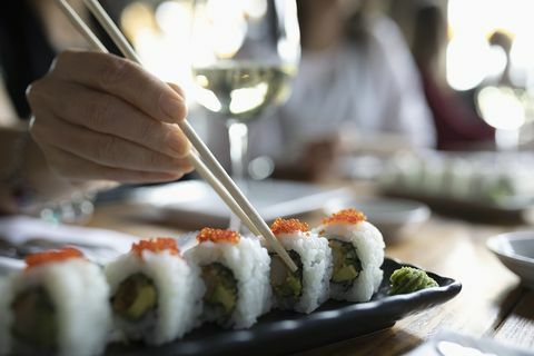 Mujer con palillos buscando sushi en la bandeja del restaurante