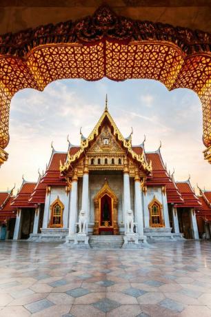 amanecer en el templo de mármol, tailandia, con un exterior de arcos y dormitorios dorados, columnas de mármol blanco y un patio de mármol con baldosas geométricas