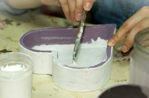 Manos pintando el interior de una caja de madera púrpura en forma de corazón blanco