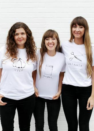 tres mujeres con camisetas blancas, con piedra, papel o tijeras escritas y representadas en la camiseta