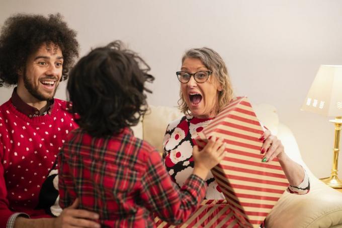 mujer mayor sentada junto al hombre en el sofá recibiendo un regalo de navidad de un niño