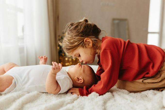 adorable niño besando a su hermanita acostada en ropa de cama blanca