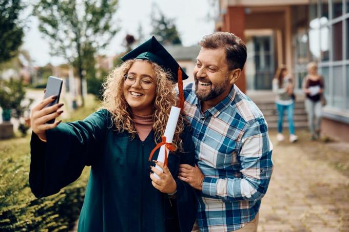 feliz graduado universitario y su padre divirtiéndose mientras toma selfie con teléfono inteligente