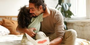 joven familia afroamericana feliz celebrando el día del padre en casa, padre amoroso abrazando a un hijo pequeño mientras recibe una tarjeta de felicitación hecha a mano con un corazón dibujado a mano para el cumpleaños