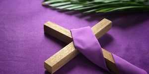 una cruz religiosa y hojas de palma sobre fondo morado