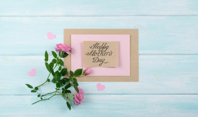 tarjeta hecha a mano con el mensaje del día de la madre en una mesa pintada de azul pálido con rosas rosas