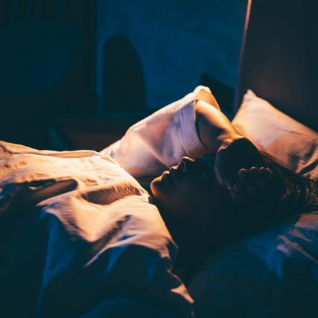 mujer con insomnio mujer joven acostada en la cama con la mano en la frente