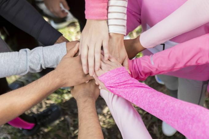 círculo de personas vestidas con camisas rosas con las manos juntas en unidad