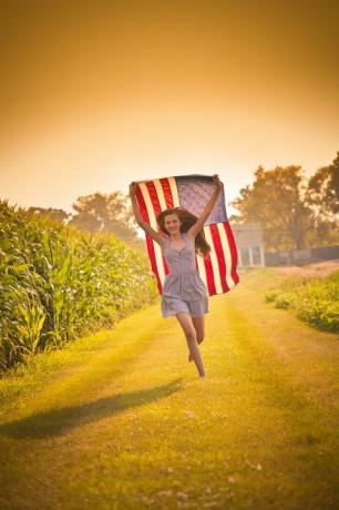jovencita adolescente corriendo por el campo ondeando la bandera estadounidense