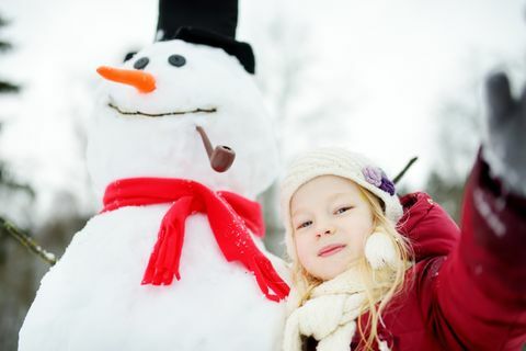 Niña adorable que construye un muñeco de nieve en parque hermoso del invierno. Lindo niño jugando en la nieve.