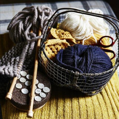 bolas de lana azul y blanca en una pequeña cesta de alambre, agujas de tejer de madera, botones, colocadas sobre tejido de punto acanalado amarillo, textura