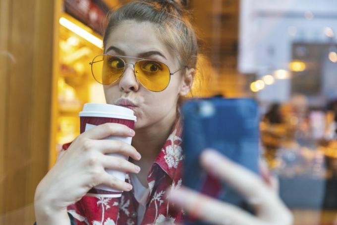 mujer joven afuera con gafas de sol tomando un selfie mientras bebe un café para ir