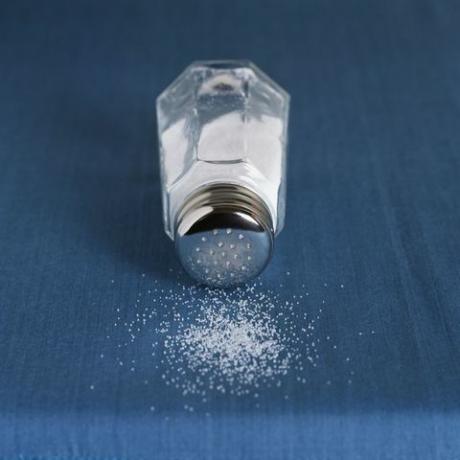 Granos de sal derramando sobre la mesa azul del recipiente de vidrio