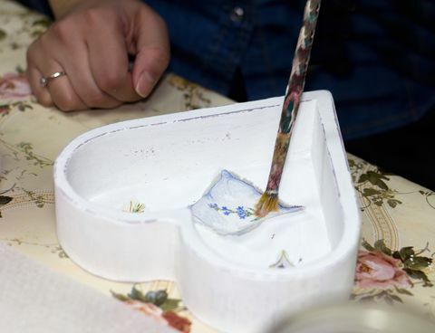 La mano de un artesano pintando una imagen recortada con pegamento en el interior de una caja blanca en forma de corazón