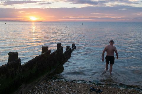 A medida que el sol se pone sobre la luz del día que se desvanece y las tranquilas aguas del estuario del Támesis, un nadador de mar salvaje entra en el agua para su chapuzón regular por la noche, el 18 de julio de 2020, en Whitstable, Kent, Inglaterra Foto de Richard Baker en imágenes a través de Getty Images