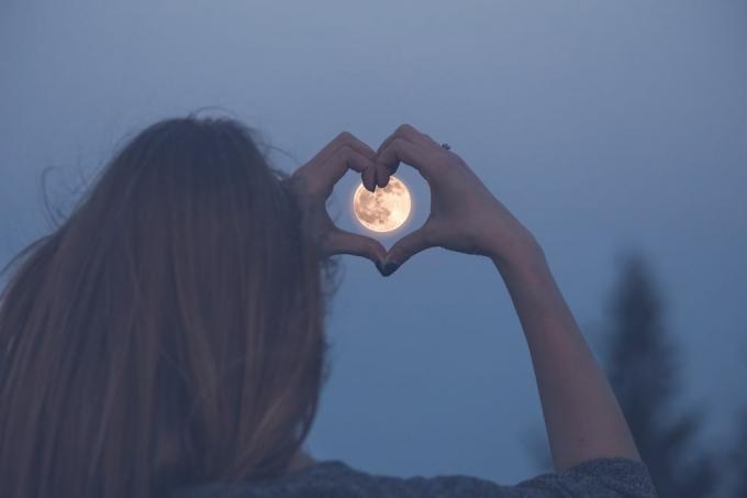 mujer haciendo forma de corazón con las manos sobre la luna llena