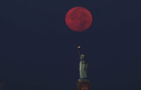 La luna llena se esconde detrás de la estatua de la libertad en la ciudad de Nueva York
