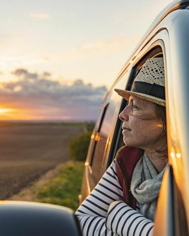 Una mujer de unos 40 años contempla la vista del campo desde su autocaravana. Se ve contenta y relajada.