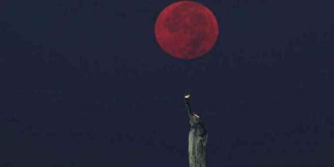 La luna llena se pone detrás de la estatua de la libertad en la ciudad de Nueva York.