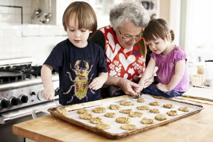 abuela y dos nietos pequeños horneando la nieta está colocando masa en una bandeja para hornear galletas con la ayuda de las abuelas