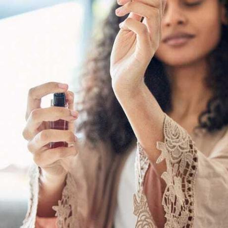 foto de una joven atractiva parada sola en casa y rociando perfume por la mañana