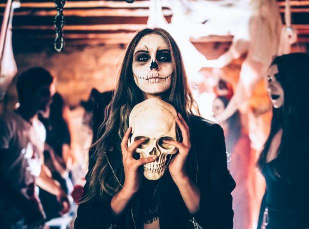 mujer joven con maquillaje de esqueleto sosteniendo el cráneo en la fiesta de halloween