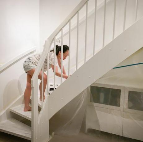 Mujer aplicando pintura blanca fresca a las escaleras.