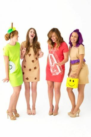 Cuatro mujeres riendo con vestidos cortos vestidas como "señoras del almuerzo", una con una lonchera amarilla con cara sonriente