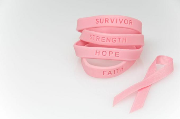 pila de pulseras de goma rosa que dicen sobreviviente, fuerza, esperanza, fe y cinta rosa al lado